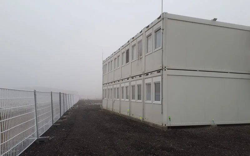 Zweigeschossige Containeranlage hinter einem Gitterzaun bei Nebel