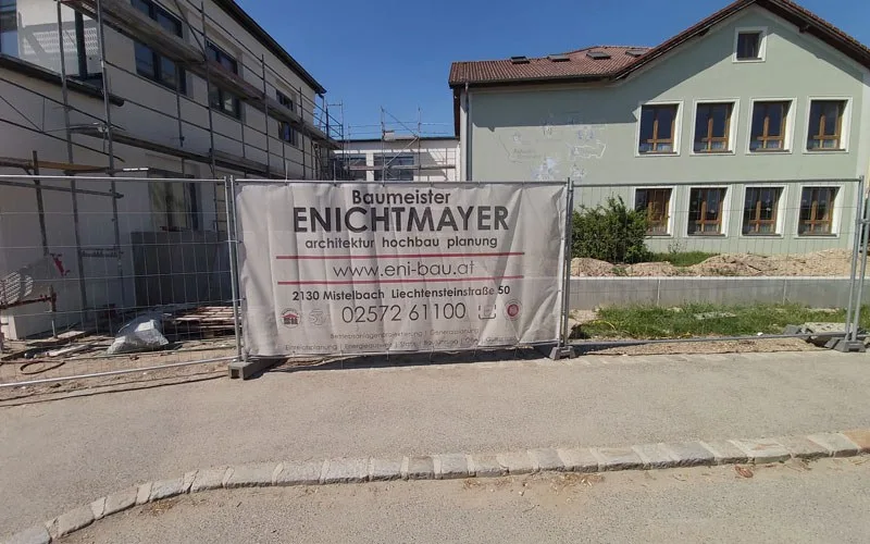 Baustelle mit Banner von Baumeister Enichtmayer vor einem Gebäude mit Gerüst