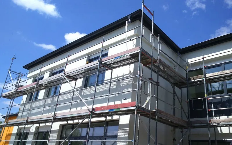 Zweigeschossiger Bau mit Gerüst an der Fassade unter blauem Himmel