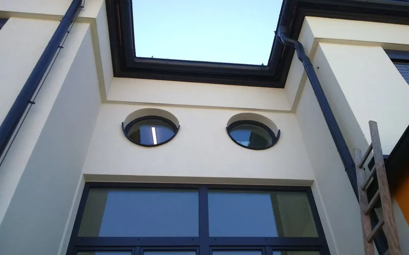 Helle Fassade mit zwei runden Fenstern über einer dunklen Fensterfront