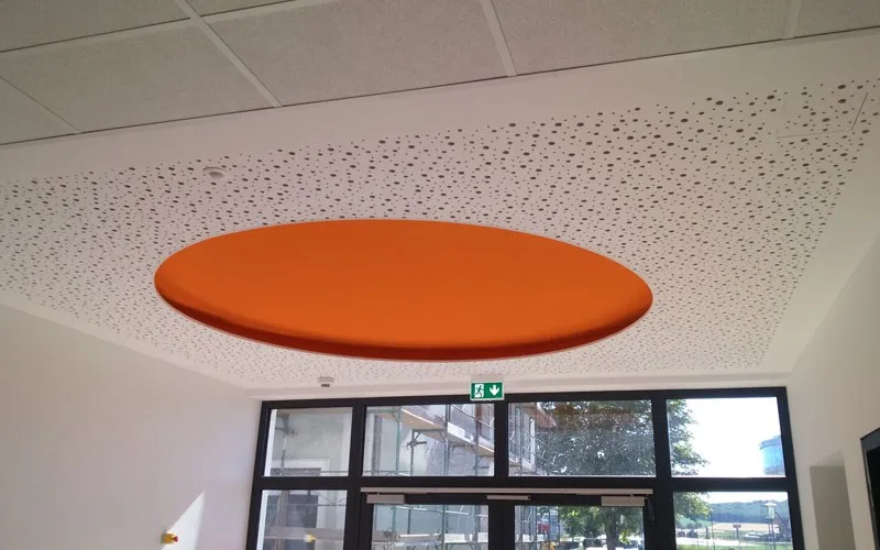 Gelochte Akustikdecke mit rundem orangem Deckensegel über einer Glasfront